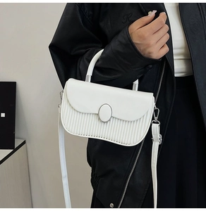 Detailed view of white pleated handbag with silver oval clasp and leather strap