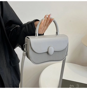 Close-up of light grey handbag with unique pleated texture and silver hardware details