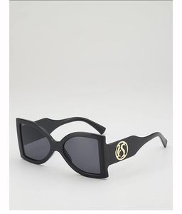 Detail of wide black sunglasses frame featuring a golden circular S logo plate on the temple
