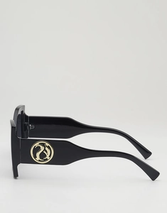 Detail of oversized black sunglasses featuring hollow gold metal logo on wide temples