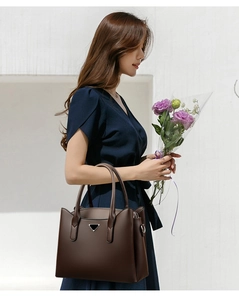 Detail of dark brown pebble leather tote bag featuring a triangular metal logo and dual handles