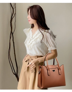 Detail of a brown textured faux leather tote bag with dual handles and metal logo plate