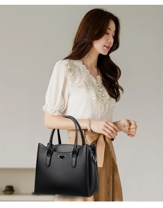 Detail of black pebbled leather tote bag featuring a triangle metal logo and sturdy handles