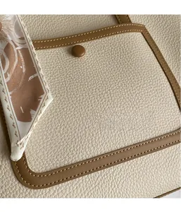 Dettaglio della borsa tote con motivo litchi, bordo marrone, fibbia magnetica e foulard