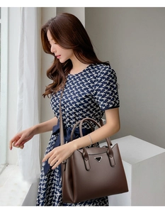 Detail of dark brown leather handbag featuring a triangular logo and textured lychee grain