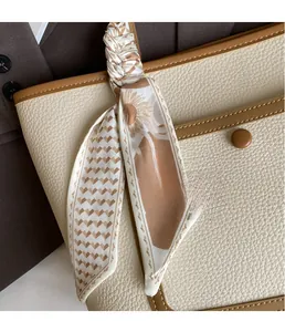 Dettaglio foulard in seta con motivi geometrici legato al manico della borsa in pelle beige