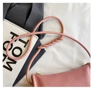 Detailed close-up of pink litchi grain leather bag with woven knot shoulder strap and gold zipper