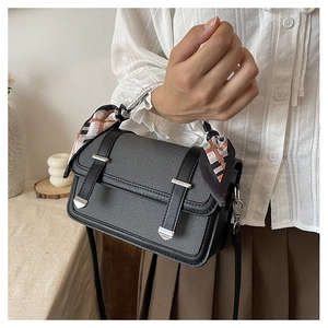 Close-up of textured fabric crossbody bag with decorative silk scarf on handle