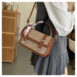 Detail of retro shoulder bag with woven canvas texture and decorative scarf on handle