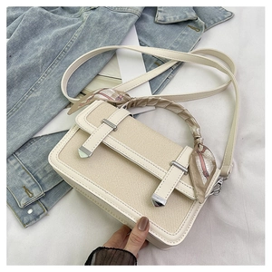 Detail of beige canvas shoulder bag with silk scarf handle and silver buckle accents