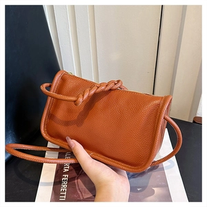 Detail of caramel crossbody bag featuring a unique twisted woven handle and lychee texture
