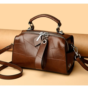 Detail of dark brown leather Boston bag showing geometric patchwork and metal zipper closure