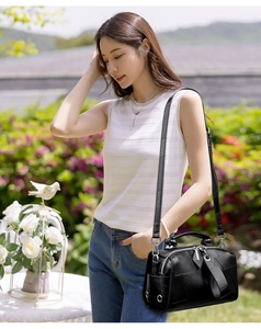 Detail of black pebbled leather crossbody pillow bag with handle and metallic eyelets
