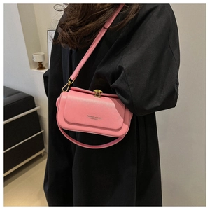 Detailed view of pink leather crossbody bag with gold hardware on a model with black coat
