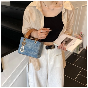 Detailed shot of denim handbag with brown leather handle and elegant pearl bow charm