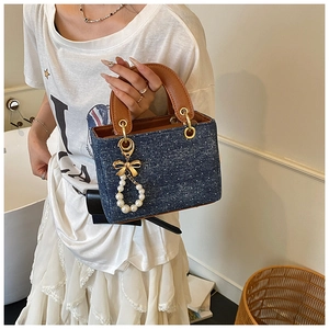 Detail of blue polka dot denim handbag with brown leather handle and pearl bow charm