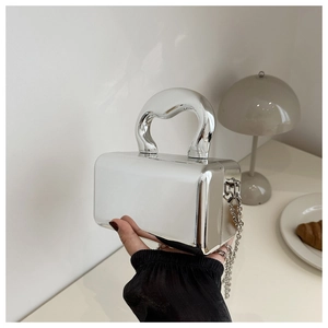 Détail du sac boîte argenté avec poignée incurvée et bandoulière chaîne sur table