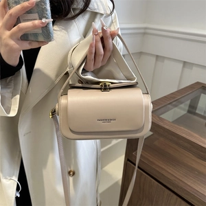 Elegant beige leather box bag with gold buckle shown in a minimalist interior setting