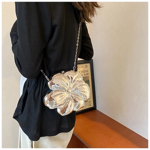 Detail of silver metallic flower crossbody bag with chain strap on a model