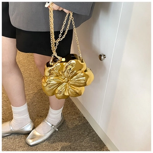 Detailed view of shiny gold flower-shaped hard shell clutch with fine metal chain strap