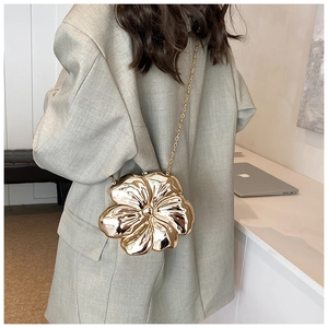 Golden flower evening clutch bag with metal chain shown on model wearing a green suit