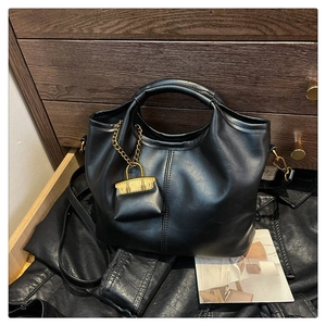 Black matte leather bag detail featuring a decorative gold chain mini charm and strap