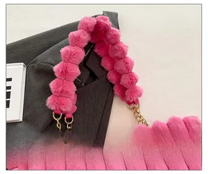 Detail of pink faux fur pom-pom shoulder strap with gold metal chain for handbags