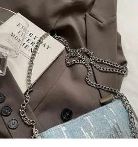 Detail of light blue denim crossbody bag with silver sequin stripes on a blazer