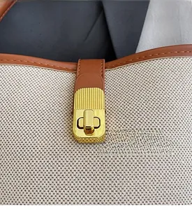 Close-up of beige canvas bag with brown leather trim and rectangular gold metal twist lock