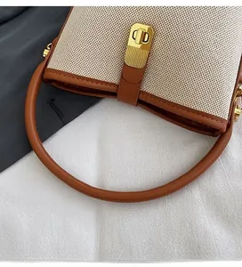 Detail of canvas bucket bag with brown leather handle and gold twist-lock closure