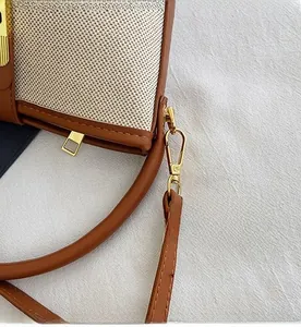 Detail of gold metal hooks and stitching on a canvas and brown leather bucket bag
