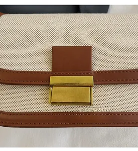 Close-up of beige woven canvas handbag with brown leather trim and golden metal clasp