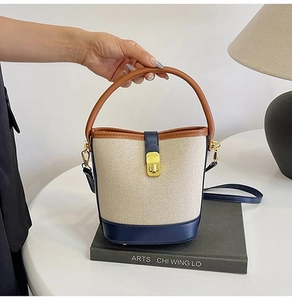 Detail of canvas bucket bag with navy leather trim, contrast stitching, and gold metal lock