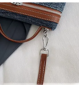 Detail of denim bag showing contrast stitching, brown leather trim and silver metal hooks