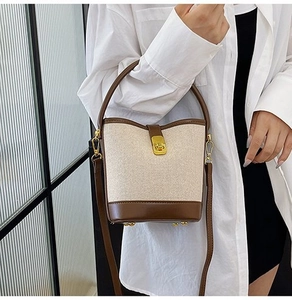 Detail of contrast stitching bucket bag with metal buckle and cream canvas texture