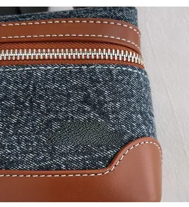 Detail view of denim and brown leather stitching with white threads and silver metal zipper