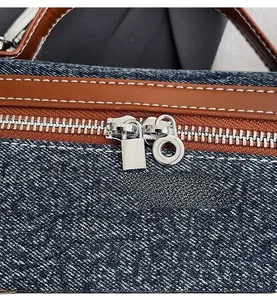 Close-up of dual silver zippers and brown leather trim on vintage denim handbag