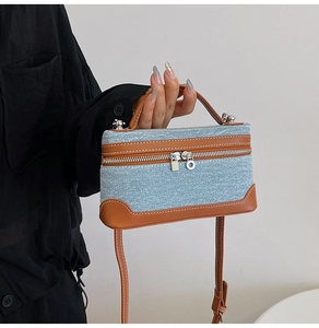 Detail of denim handbag with contrast brown leather trim and dual metal zippers