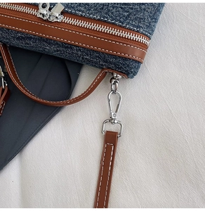 Close-up of double silver zippers and stitching detail on denim shoulder bag