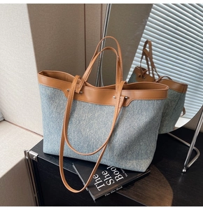 Close-up of a large denim tote bag with brown leather handles and silver metal rivets
