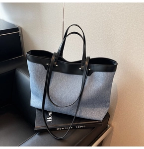 Detail of blue denim tote bag with black leather handles on a leather sofa