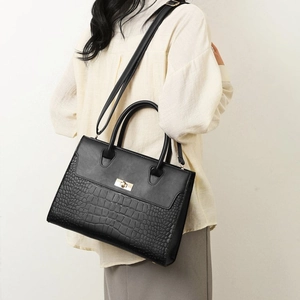 Detail of black tote with crocodile texture, gold rotary lock and adjustable strap