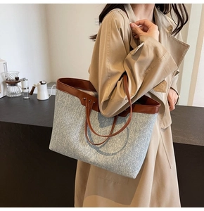 Close-up of large tote bag with blue canvas and brown leather straps in a cafe setting