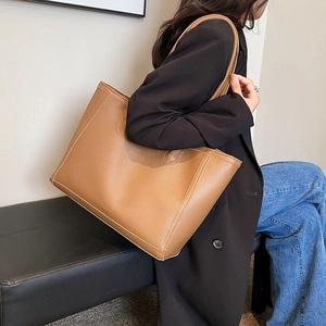 Brown lychee leather tote bag shown on a model wearing a black blazer and denim jeans