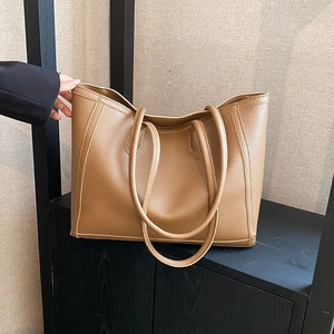 Detail of tan pebble leather tote bag with slender straps on a dark wooden surface