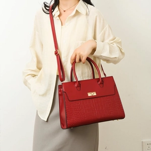 Detail of dark red leather tote featuring crocodile texture and golden clasp on the model