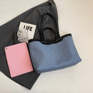 Close-up of blue denim tote bag with black leather straps and office essentials