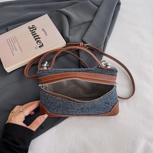 Retro denim crossbody bag with brown leather trim and white stitching on grey background