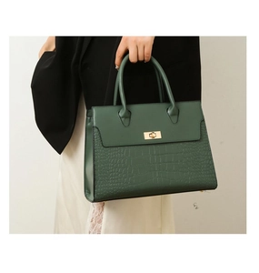 Detailed view of dark green tote with crocodile pattern texture and gold twist lock clasp