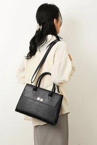 Black tote bag with faux crocodile pattern and gold twist lock on a model's shoulder